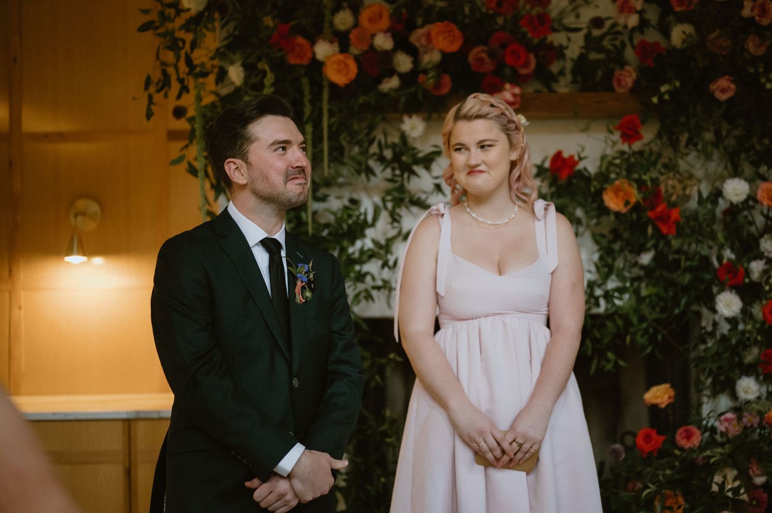 A couple stands before a lush floral arch during their wedding ceremony.