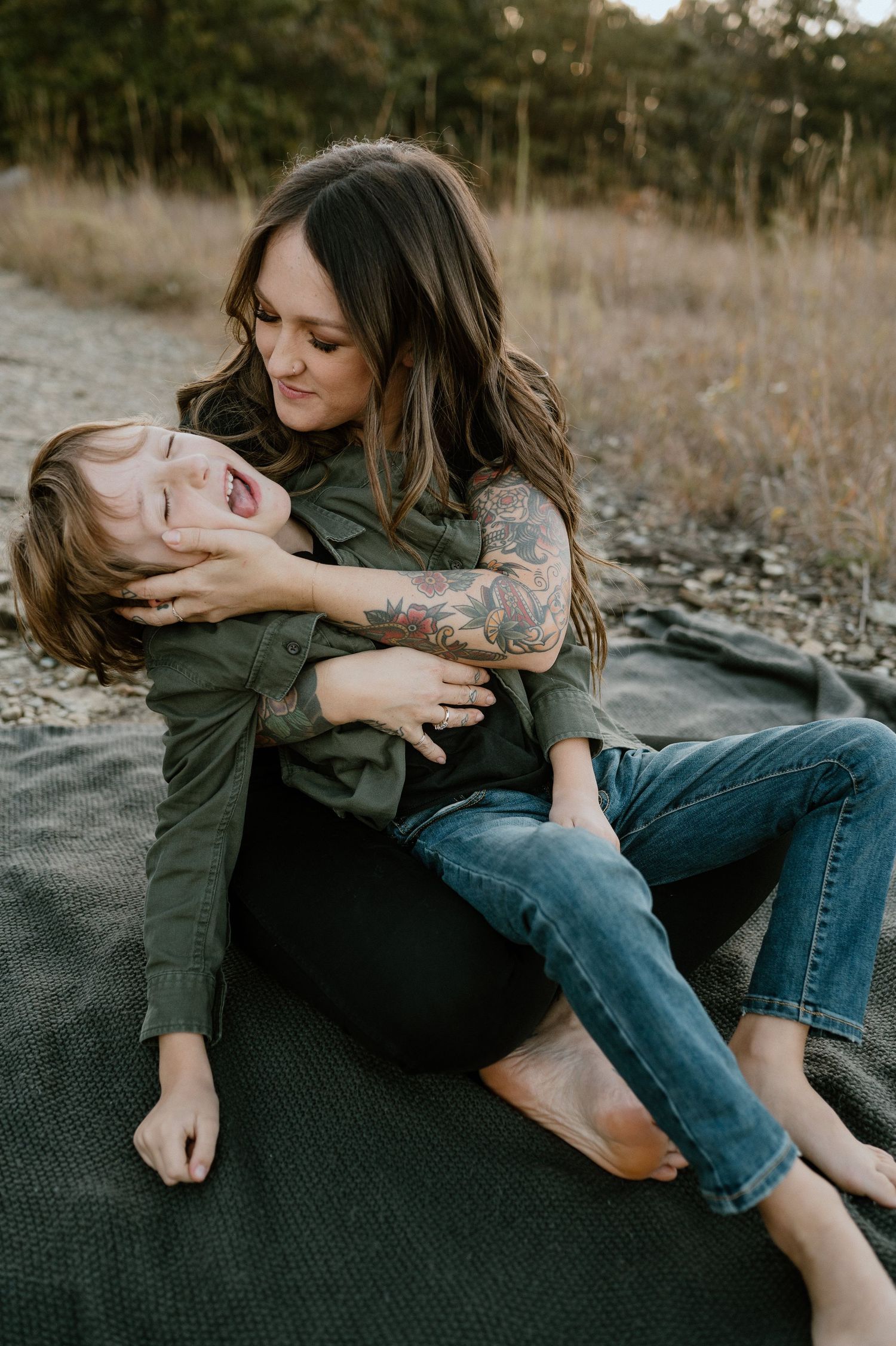 A candid moment shows parent and child laughing together while relaxing on a blanket during golden hour.
