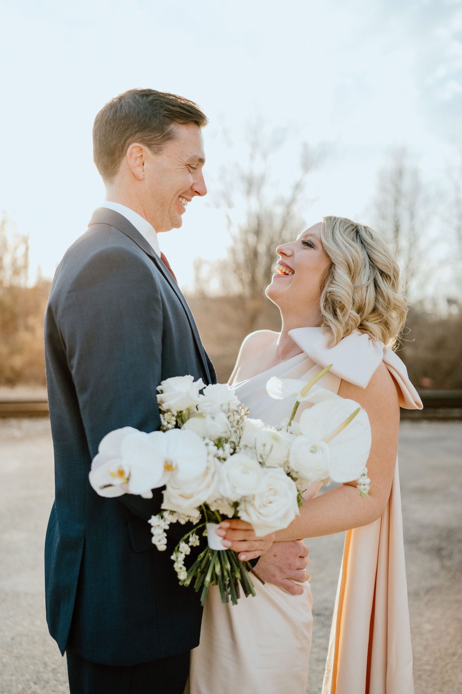 Joyful candid moment between couple sharing laughter while holding white orchid bouquet.