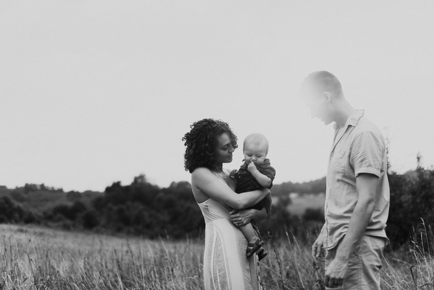Black and white portrait of a family sharing a tender moment in a meadow.
