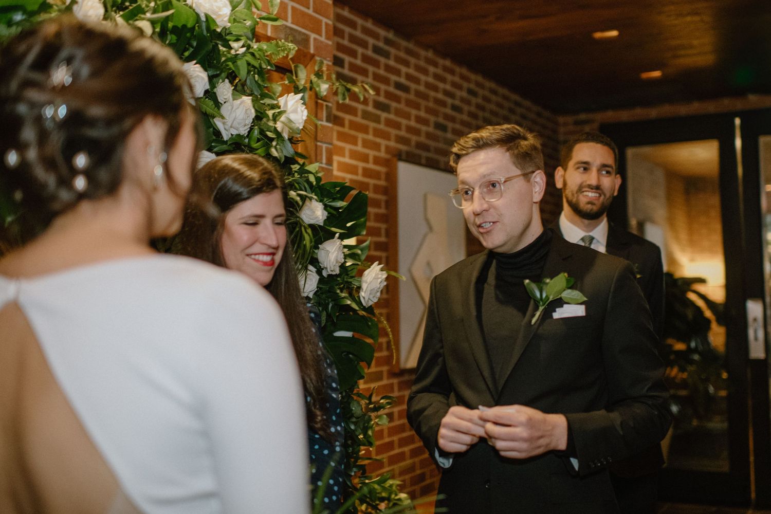 A wedding ceremony moment in an industrial-chic venue decorated with greenery and white flowers.