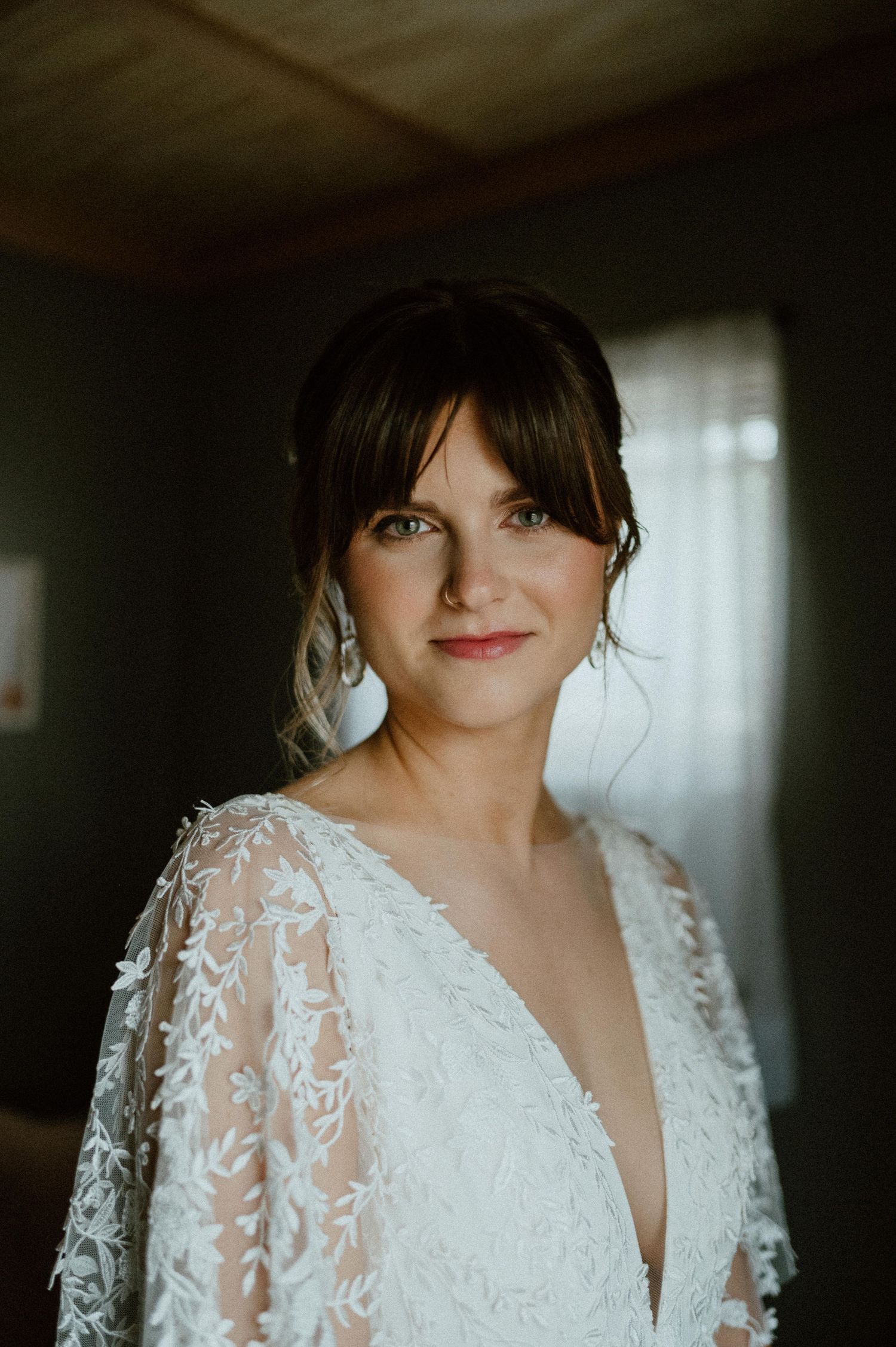 A bride poses in an elegant lace wedding gown with long sleeves and plunging neckline.