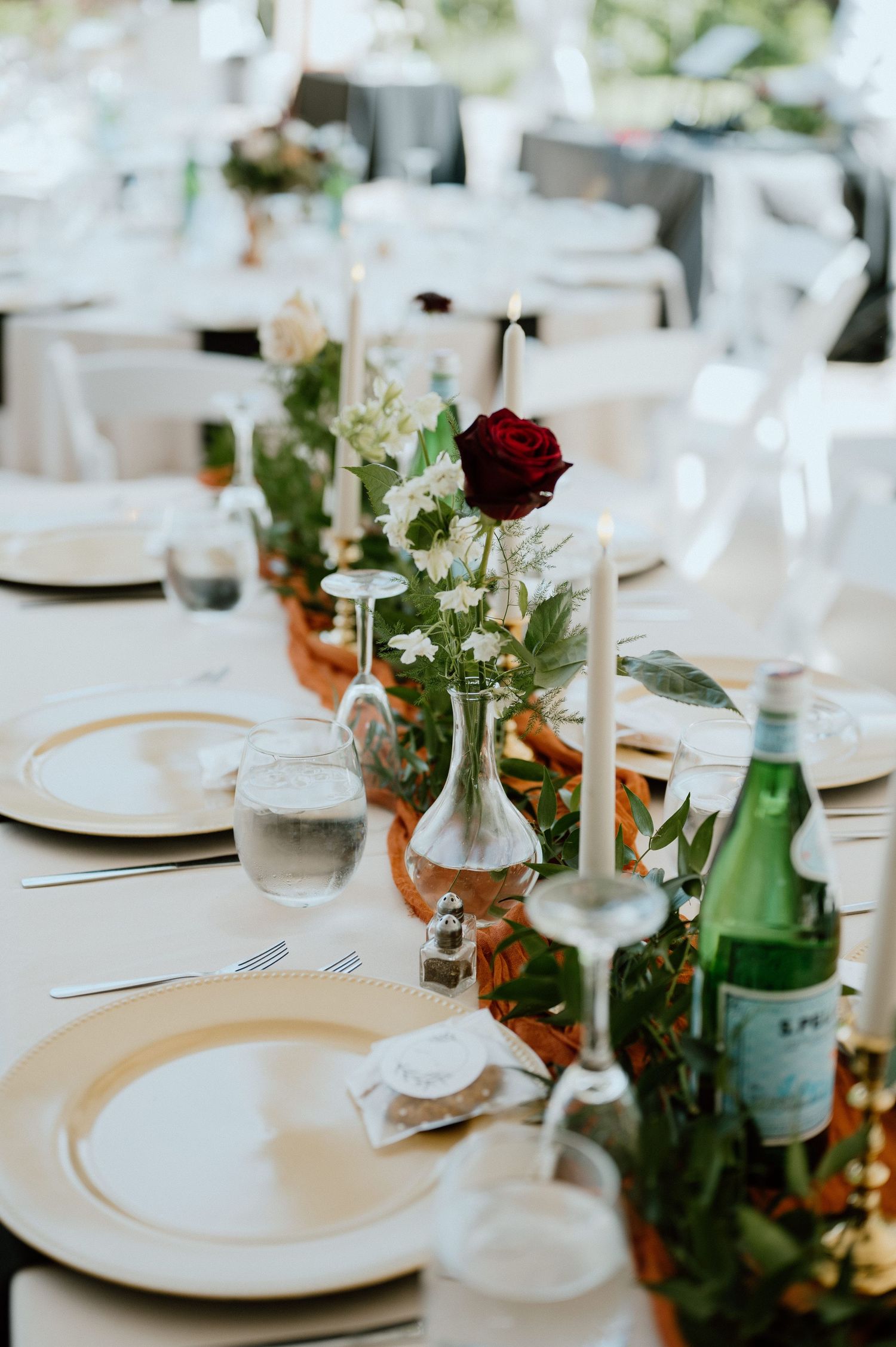 Wedding reception table with white plates, red roses, and candlesticks on a crisp white tablecloth.