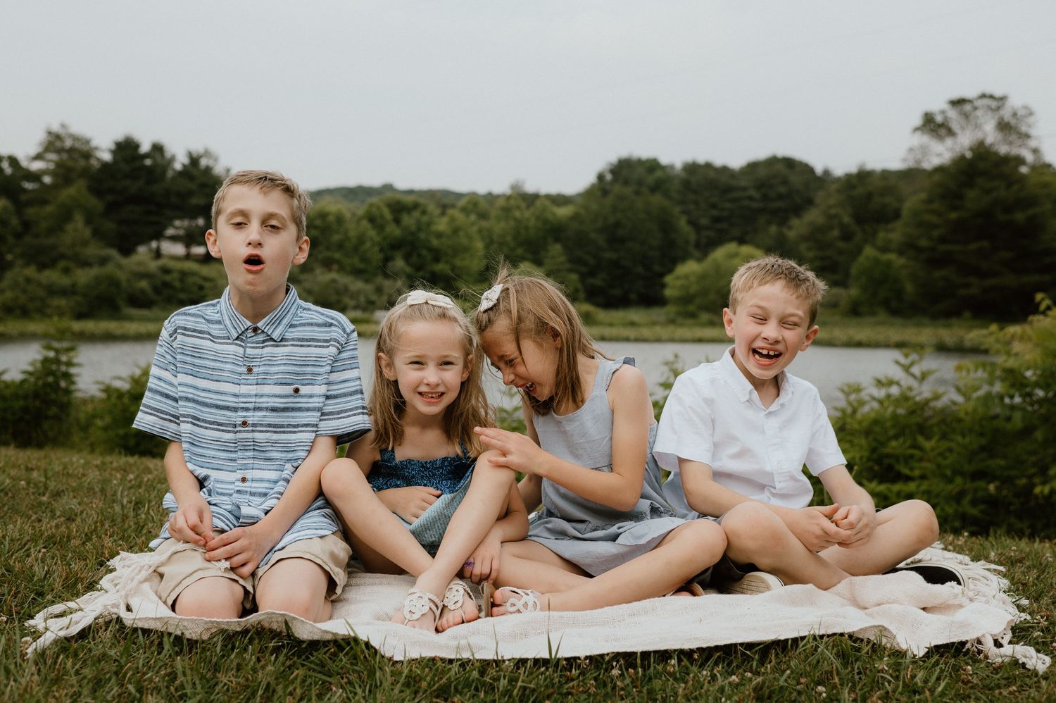 Group sitting together on blanket by lake for outdoor summer photo.