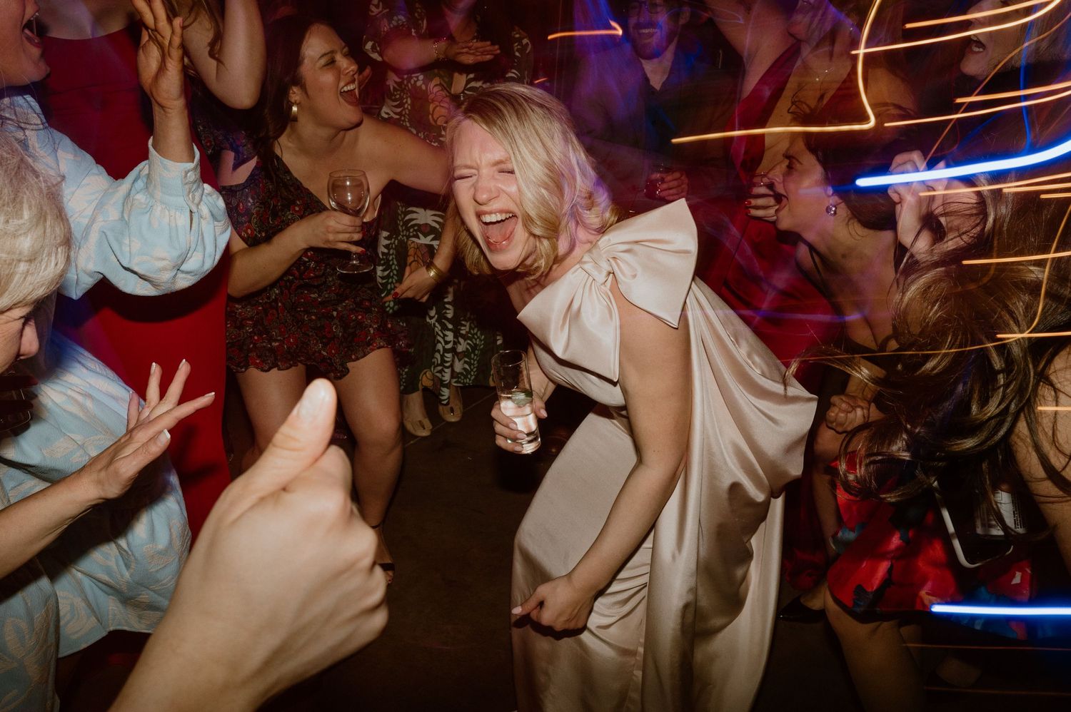 Party guests dance exuberantly under colorful lights in a dimly lit venue.