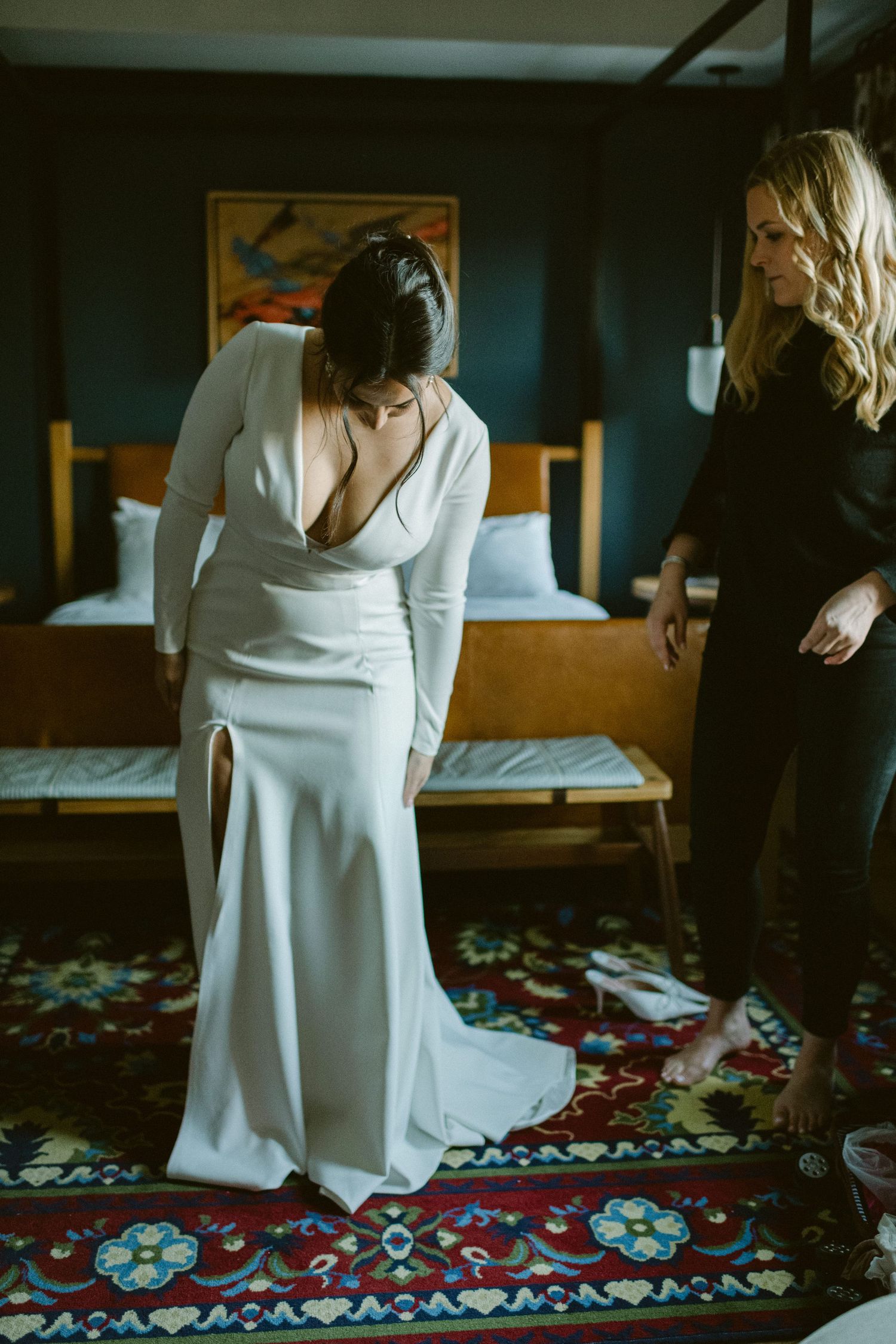 A modern bridal fitting scene in a hotel room with an elegant white wedding dress and decorative carpet.
