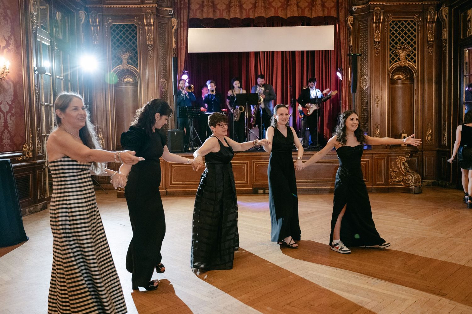 Wedding reception dance in a grand ballroom with wooden floors and elegant decor.