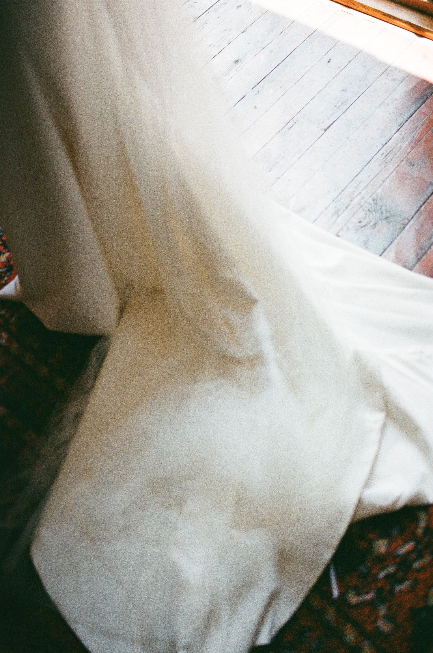 Close-up details of flowing white fabric against wooden floorboards.