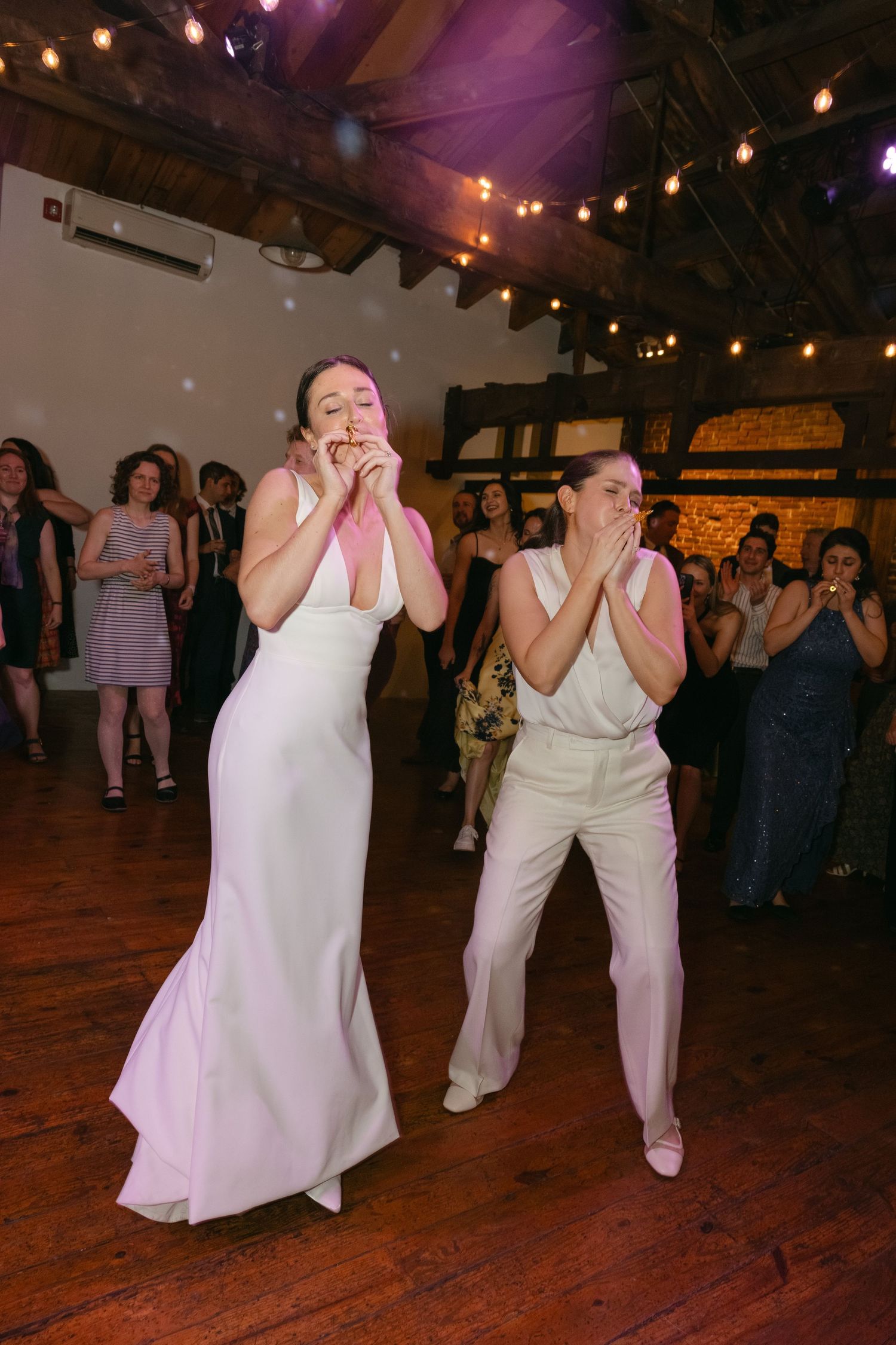 People in white attire dancing in a dimly lit venue with string lights overhead.
