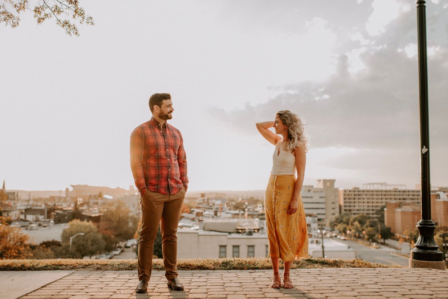 Couple poses dramatically against a city skyline backdrop during golden hour photography session.