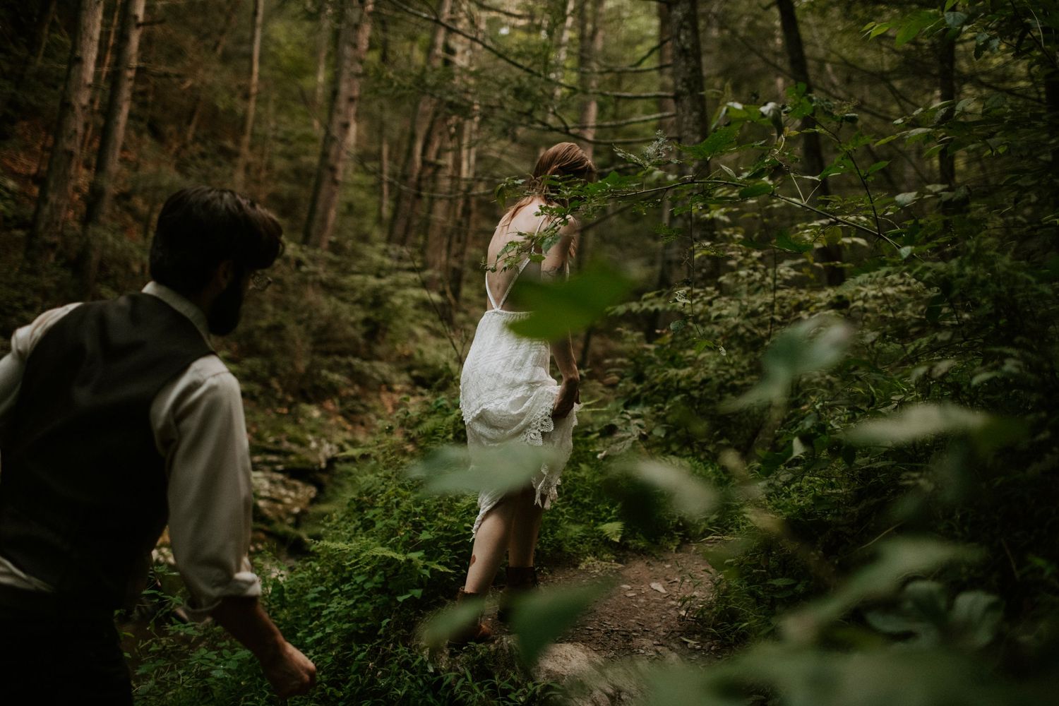 A couple enjoying a playful moment on a forest trail during their wedding photoshoot.