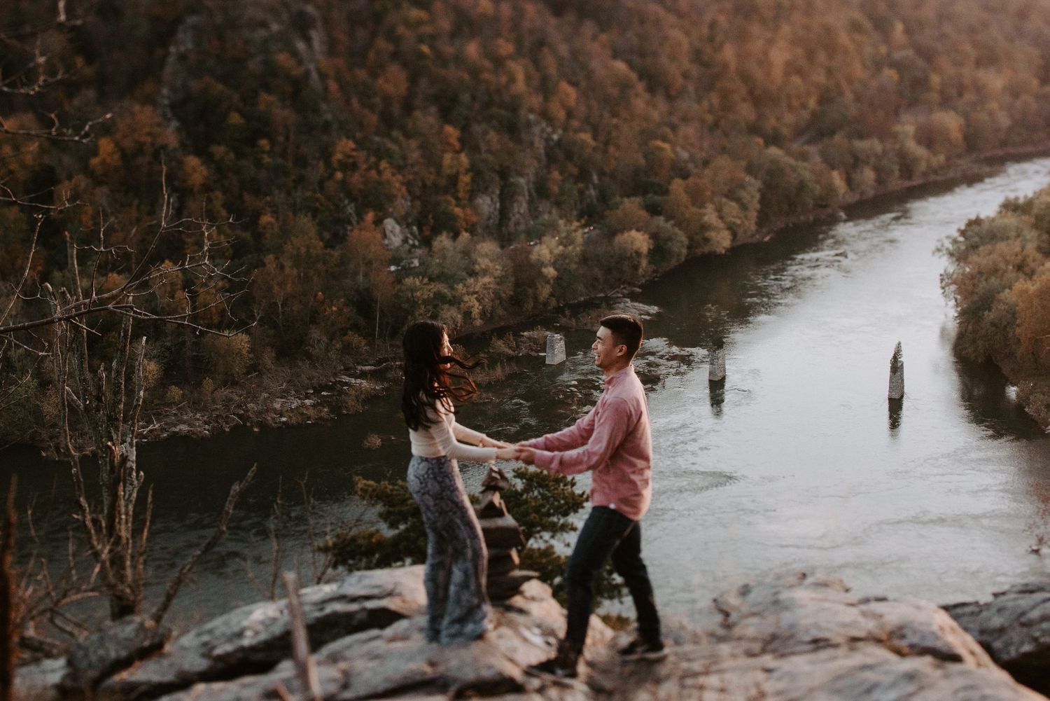 Couple standing on rocky outcrop overlooking river valley in autumn.