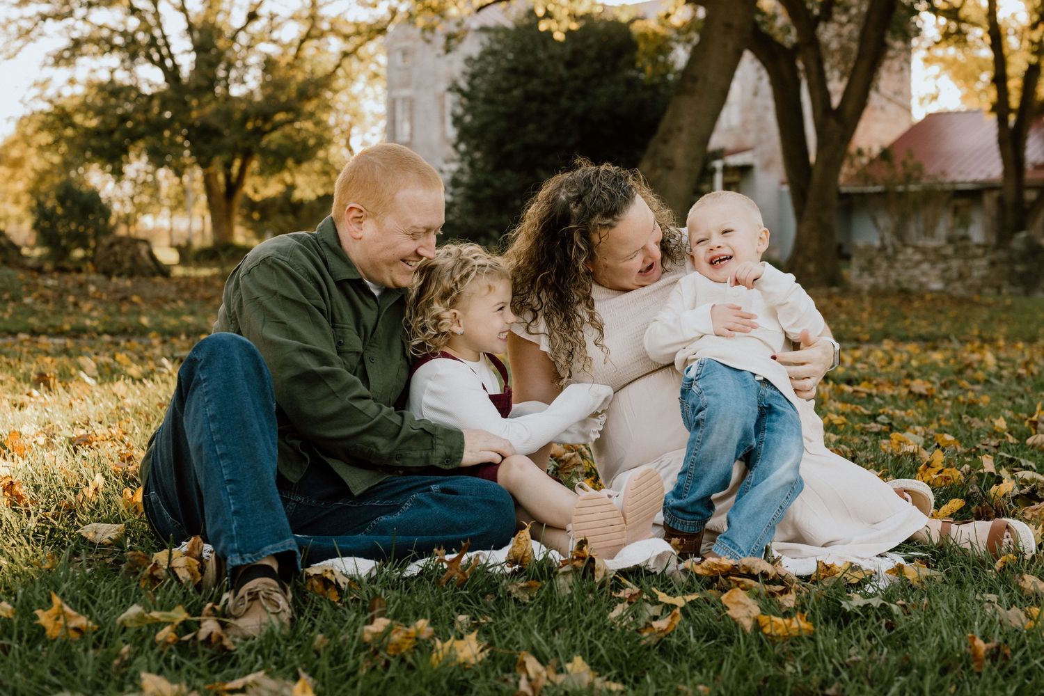 Family sitting together on blanket in autumn leaves at sunset.