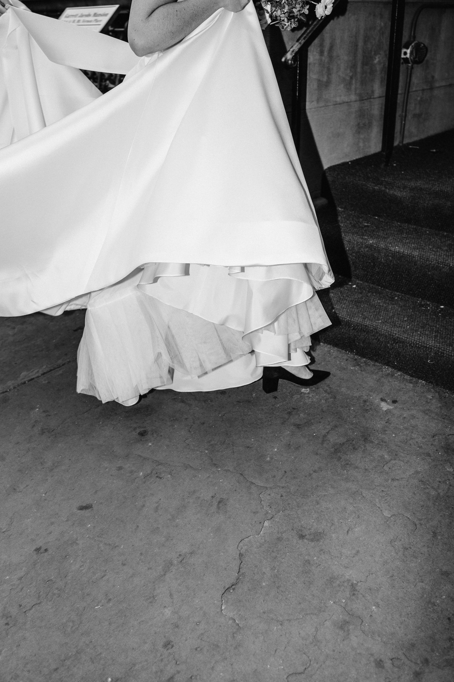 Close-up black and white photo of a wedding dress hem and shoes.
