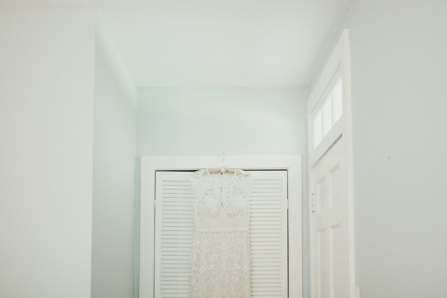 White wedding dress hanging on closet door in bright, minimalist hallway.
