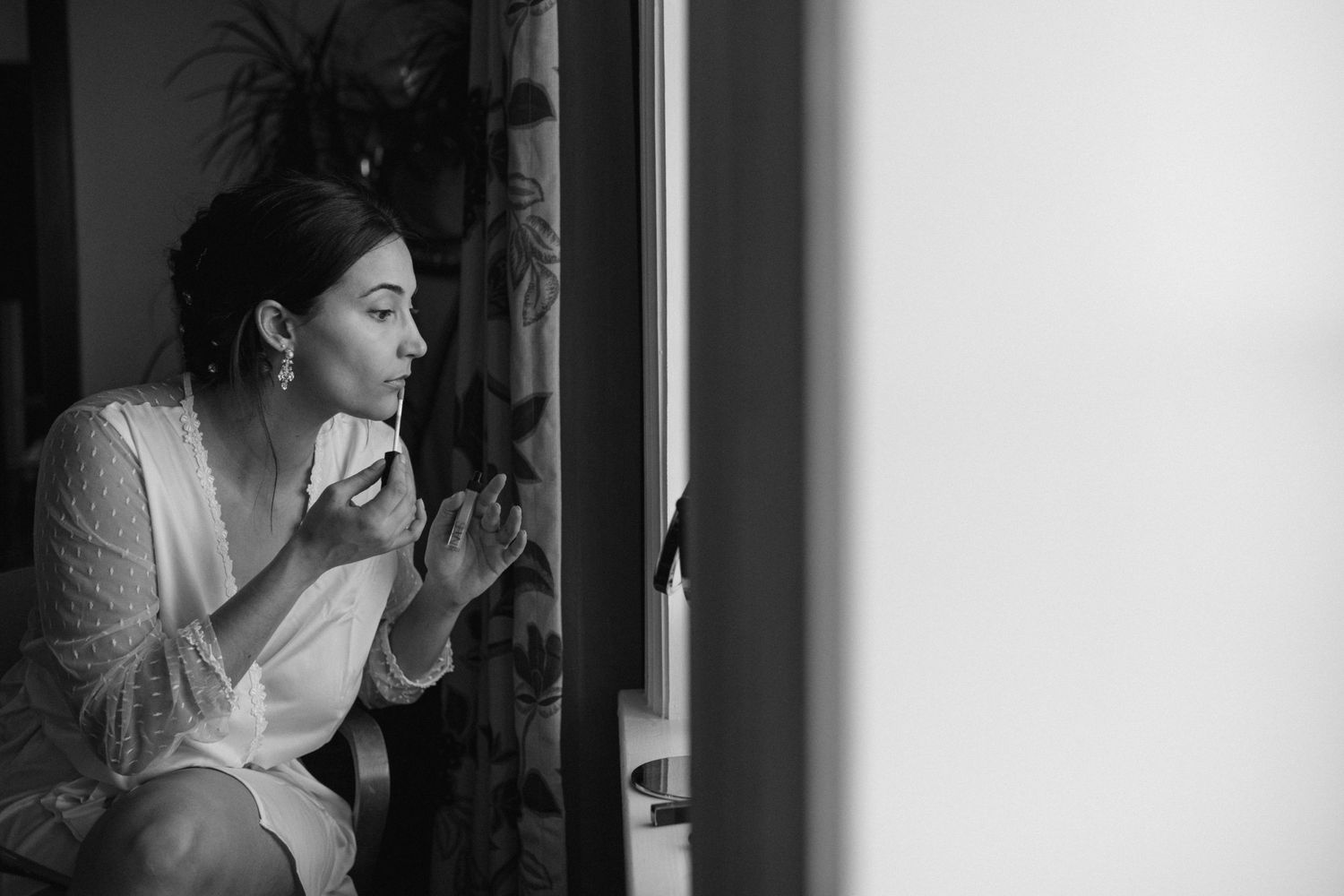 Black and white portrait of someone applying makeup by window light.