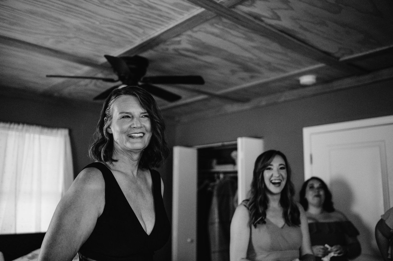 Wedding party members share joyful laughter in a sunlit room during pre-ceremony preparations.