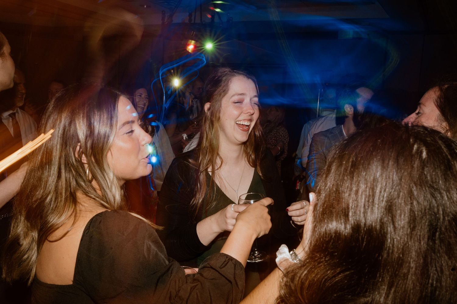 Joyful party scene with friends laughing and dancing in a dimly lit venue with colorful lights.