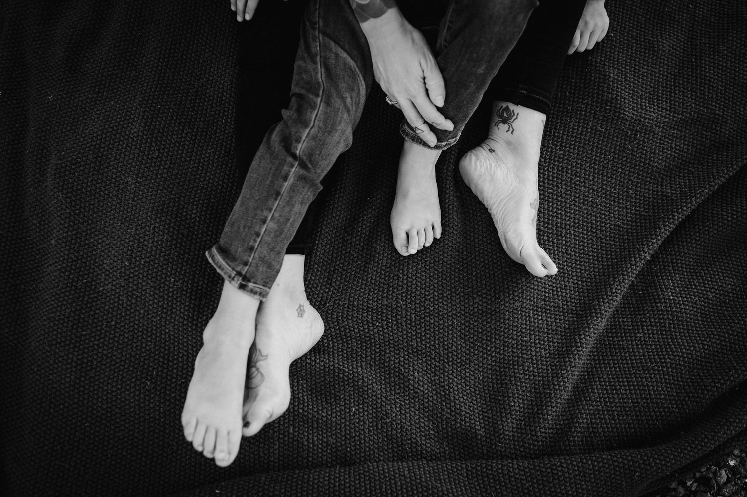 A close-up black and white image of bare feet resting on a dark fabric surface.