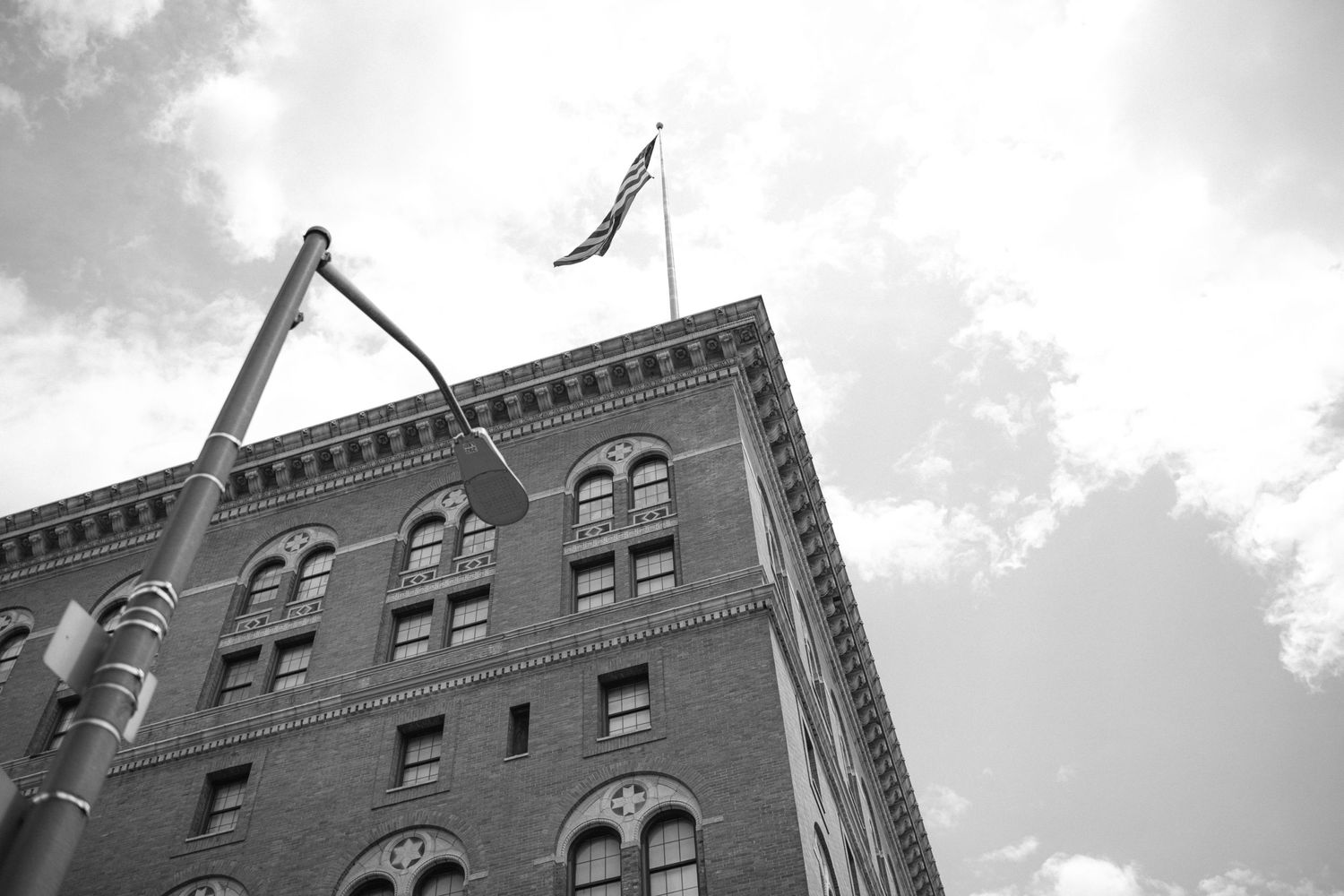 Historic brick building with arched windows and American flag shot from below against cloudy sky.