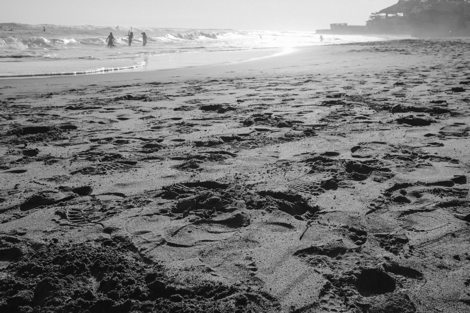 Silhouettes of beachgoers on a sandy shore at sunset with waves breaking in the background.