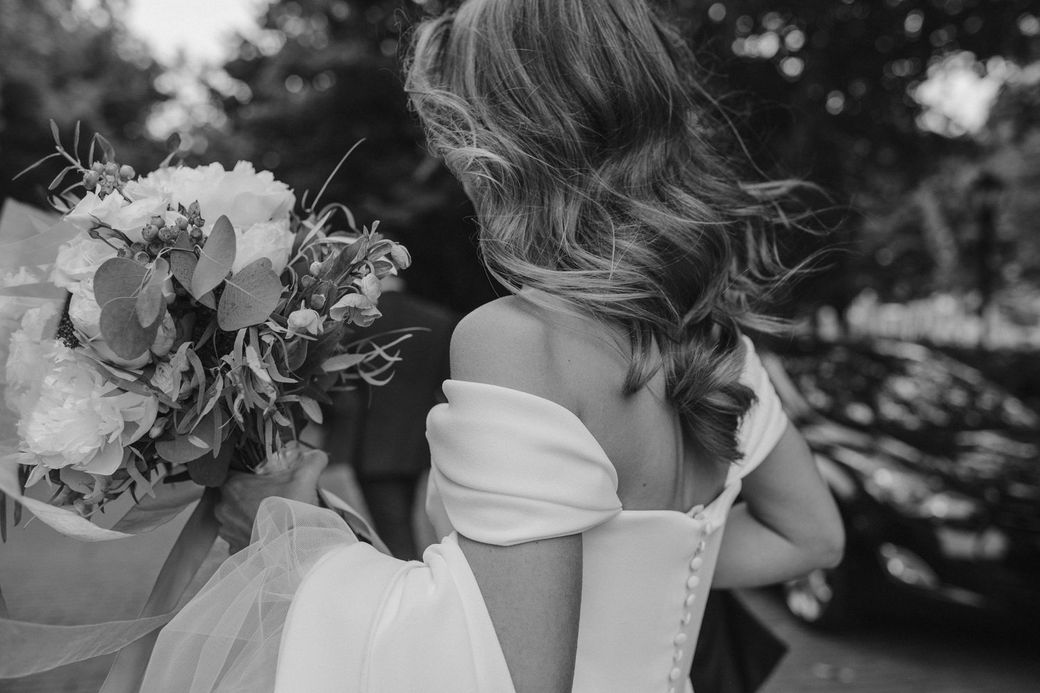 Black and white detail shot of an off-shoulder wedding dress and bouquet.