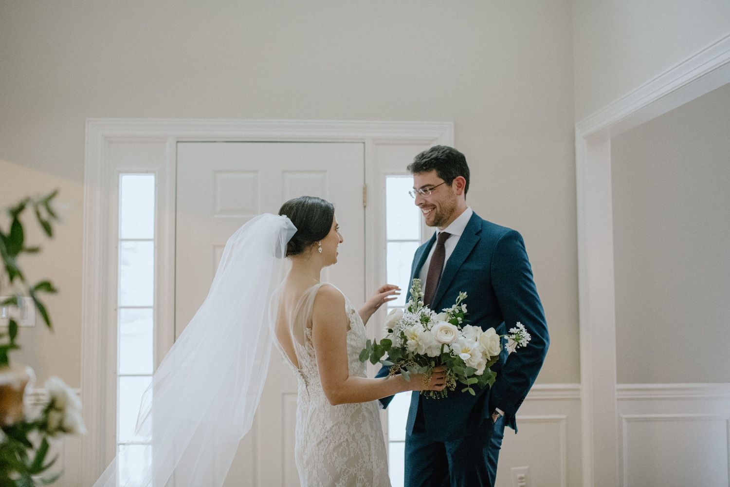 A wedding couple shares an intimate moment while holding a white floral bouquet in a bright indoor space.