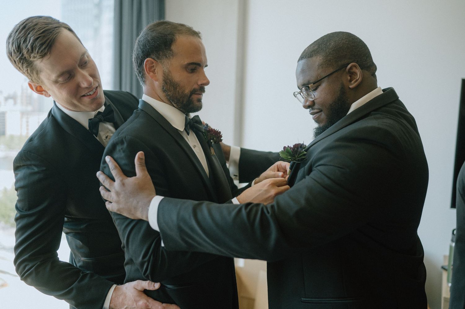 Groomsmen helping each other prepare and adjust formal attire before the ceremony.