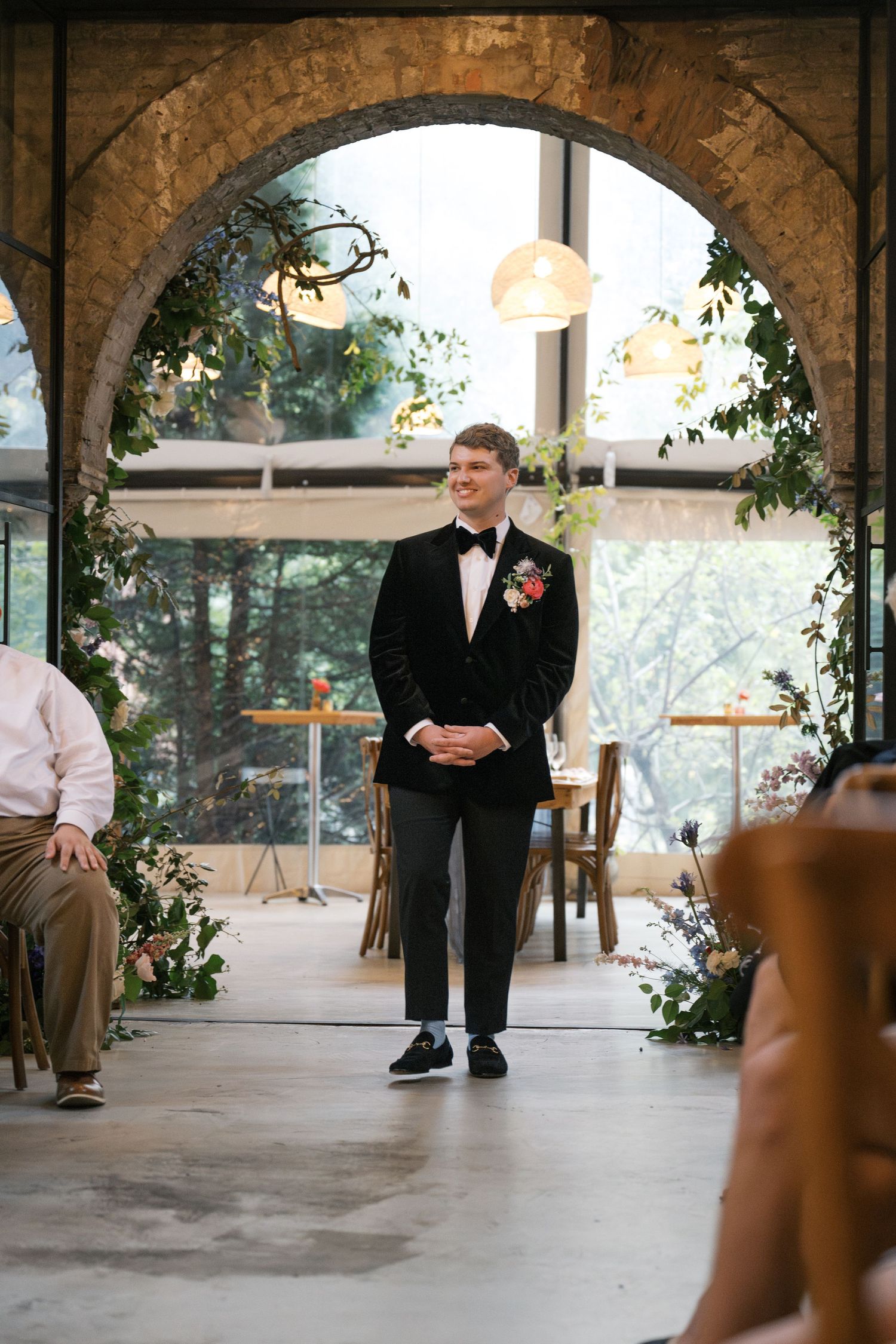 A groom stands under a decorated archway waiting at the ceremony altar.