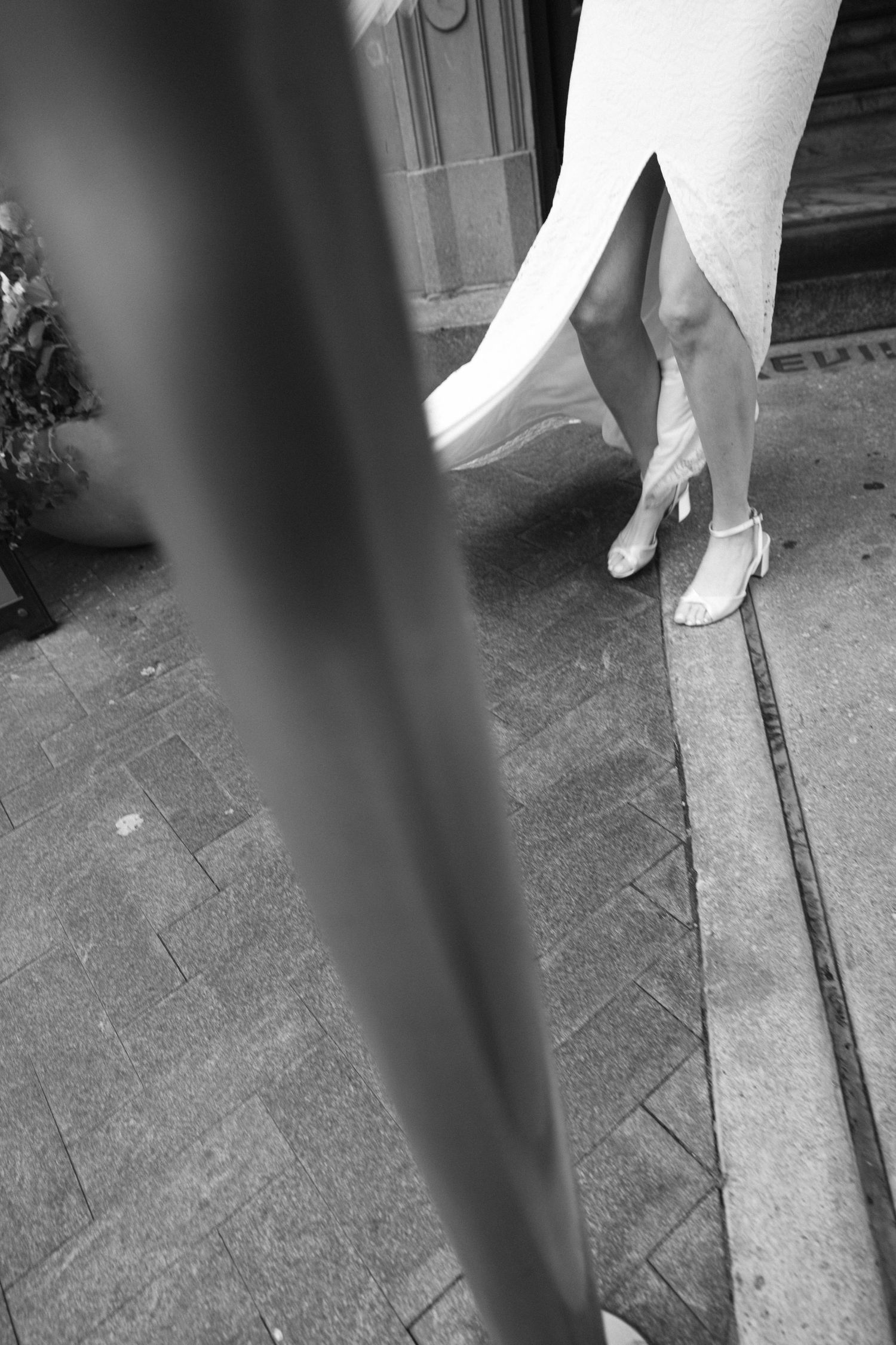 A black and white detail shot of a bride's feet in elegant shoes beneath her dress hem.