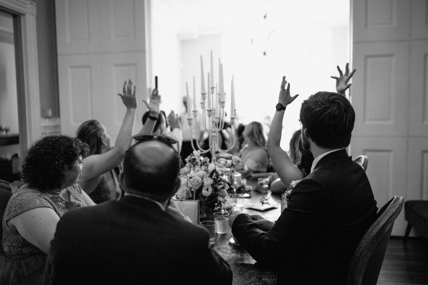 Wedding guests raising their hands in celebration at a reception dinner table with decorative candles.