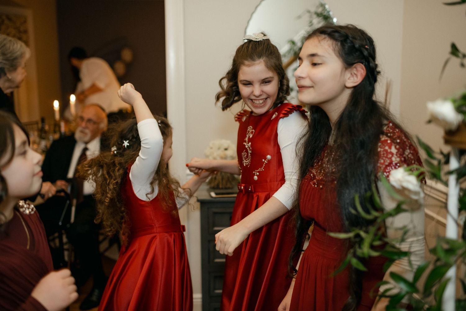 Wedding guests dancing and celebrating in red dresses at indoor reception.