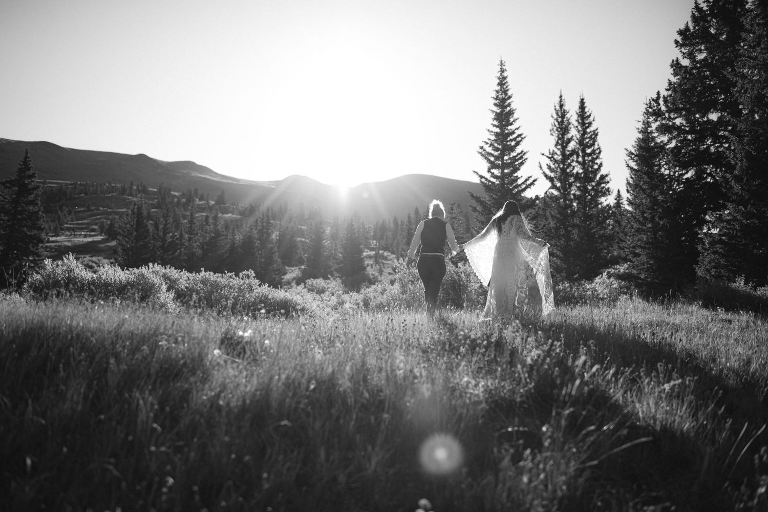 A black and white photo of two people walking through a mountain meadow at sunset.