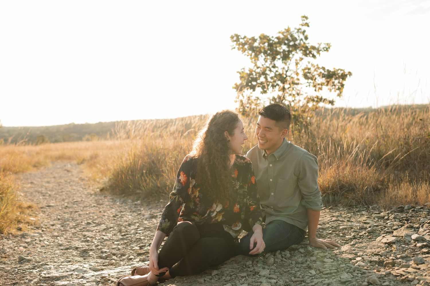 A couple sitting together on a path surrounded by golden prairie grass at sunset.
