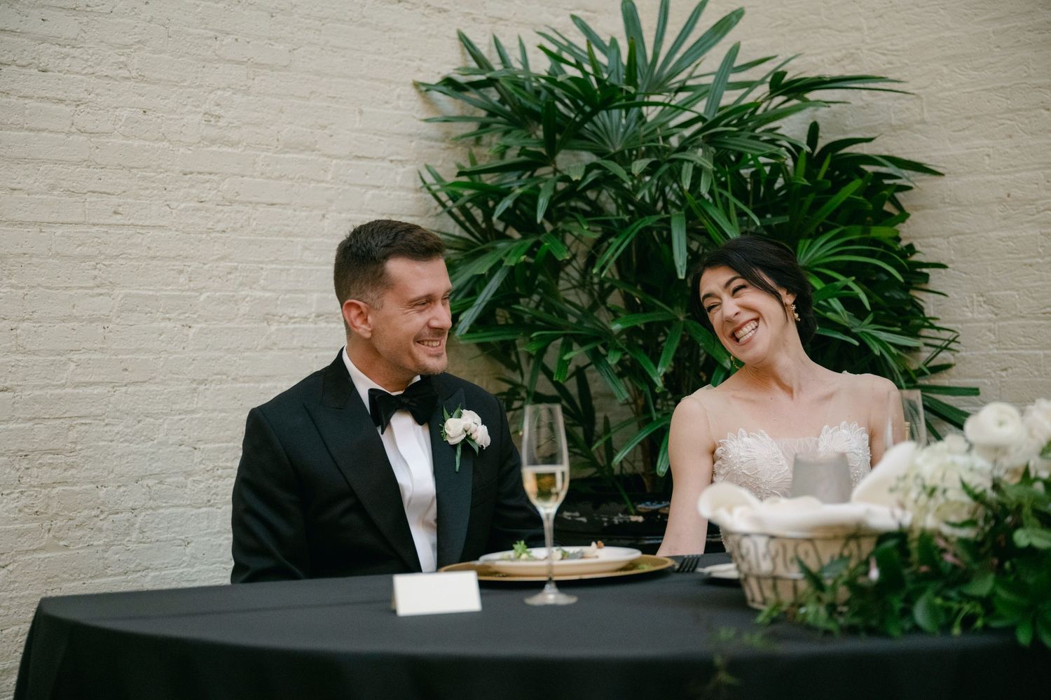Formal wedding couple sharing a moment at a black-clothed table with champagne.