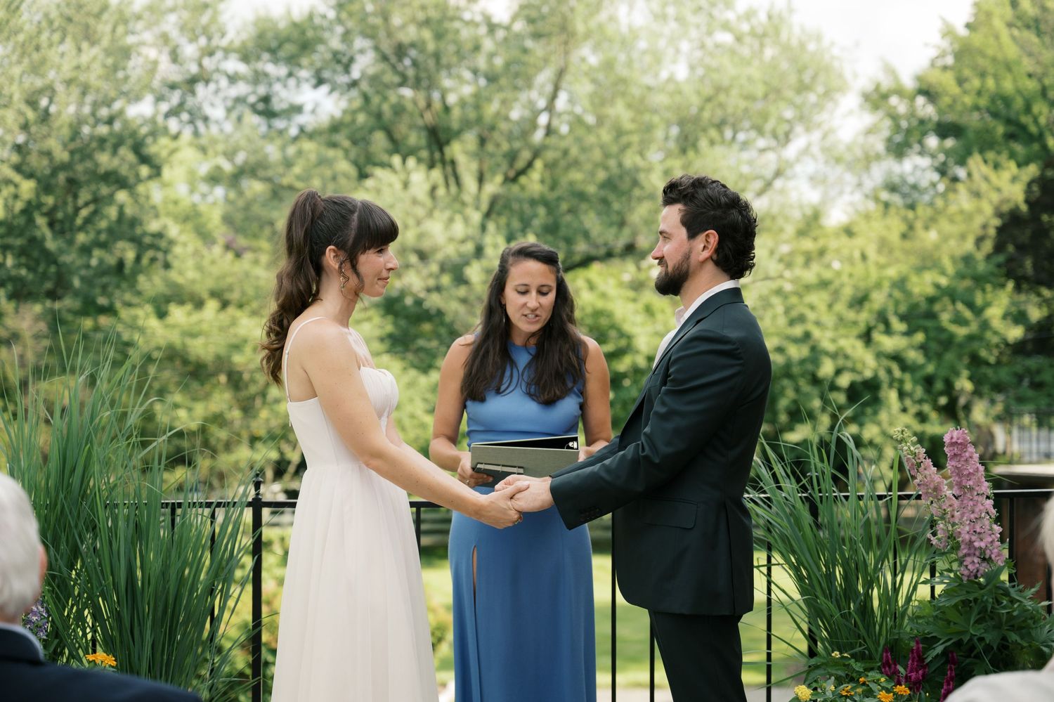 Wedding ceremony takes place in a lush garden setting with greenery and natural light.