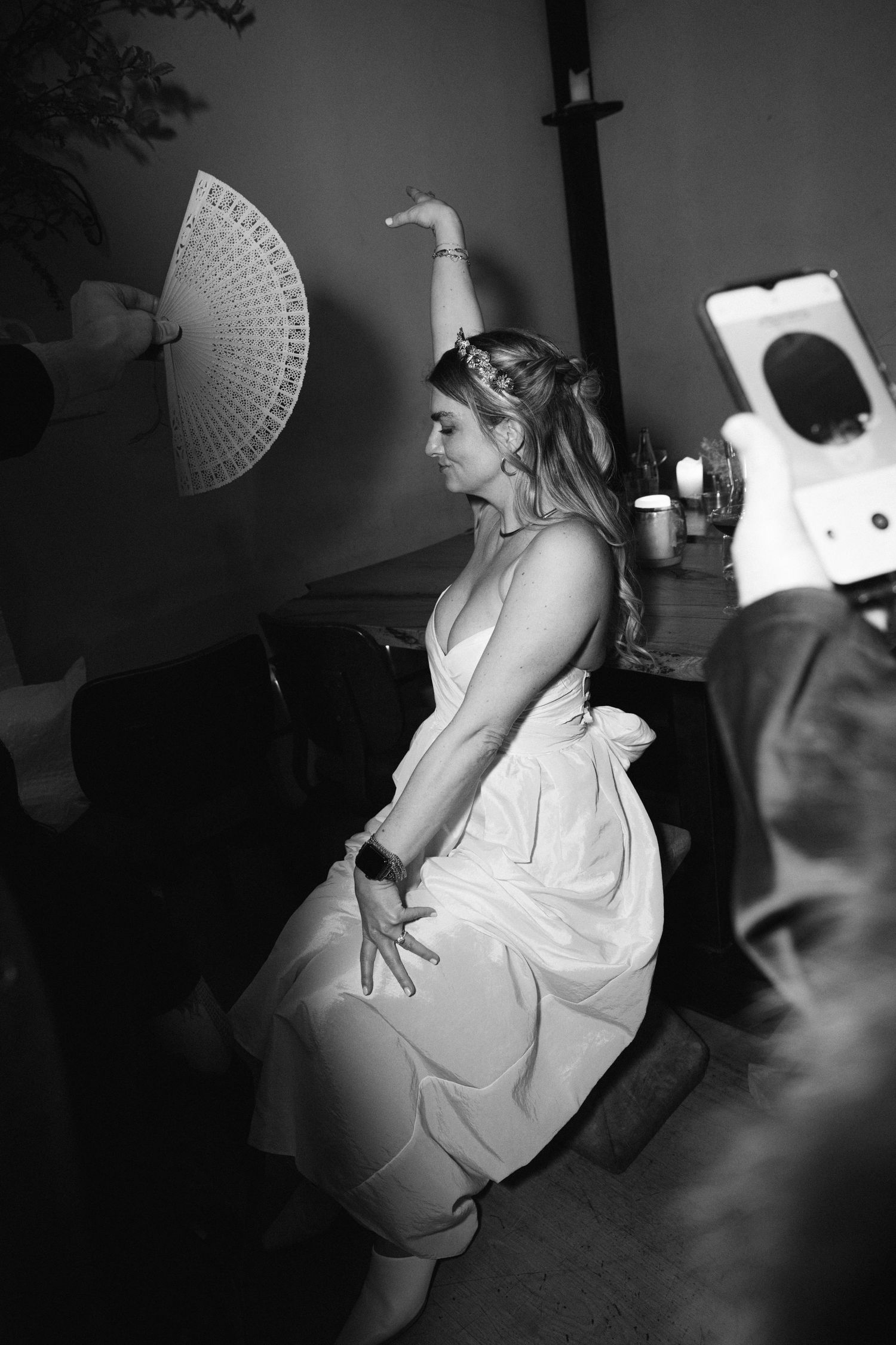 Behind the scenes black and white photo of dancer in white dress striking dramatic pose with fan in studio setting.