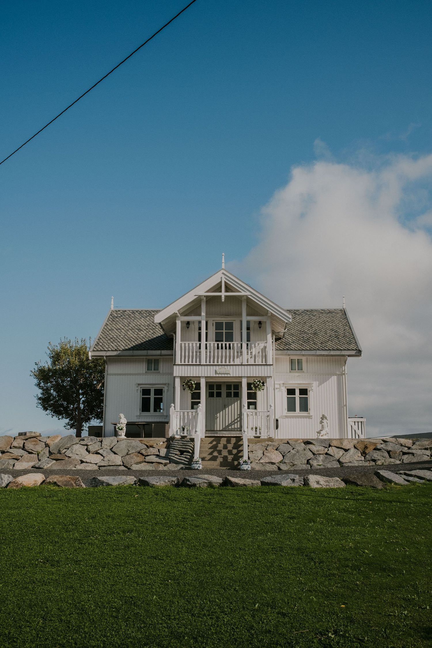 Traditional white Norwegian house with stone foundation and balcony set against blue sky.