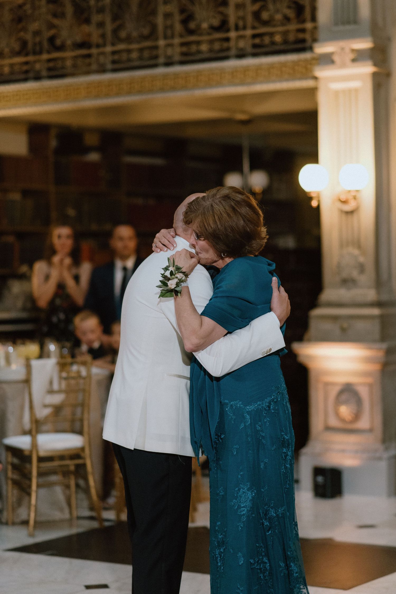 Intimate embrace between two wedding guests dancing on checkered floor of historic library.