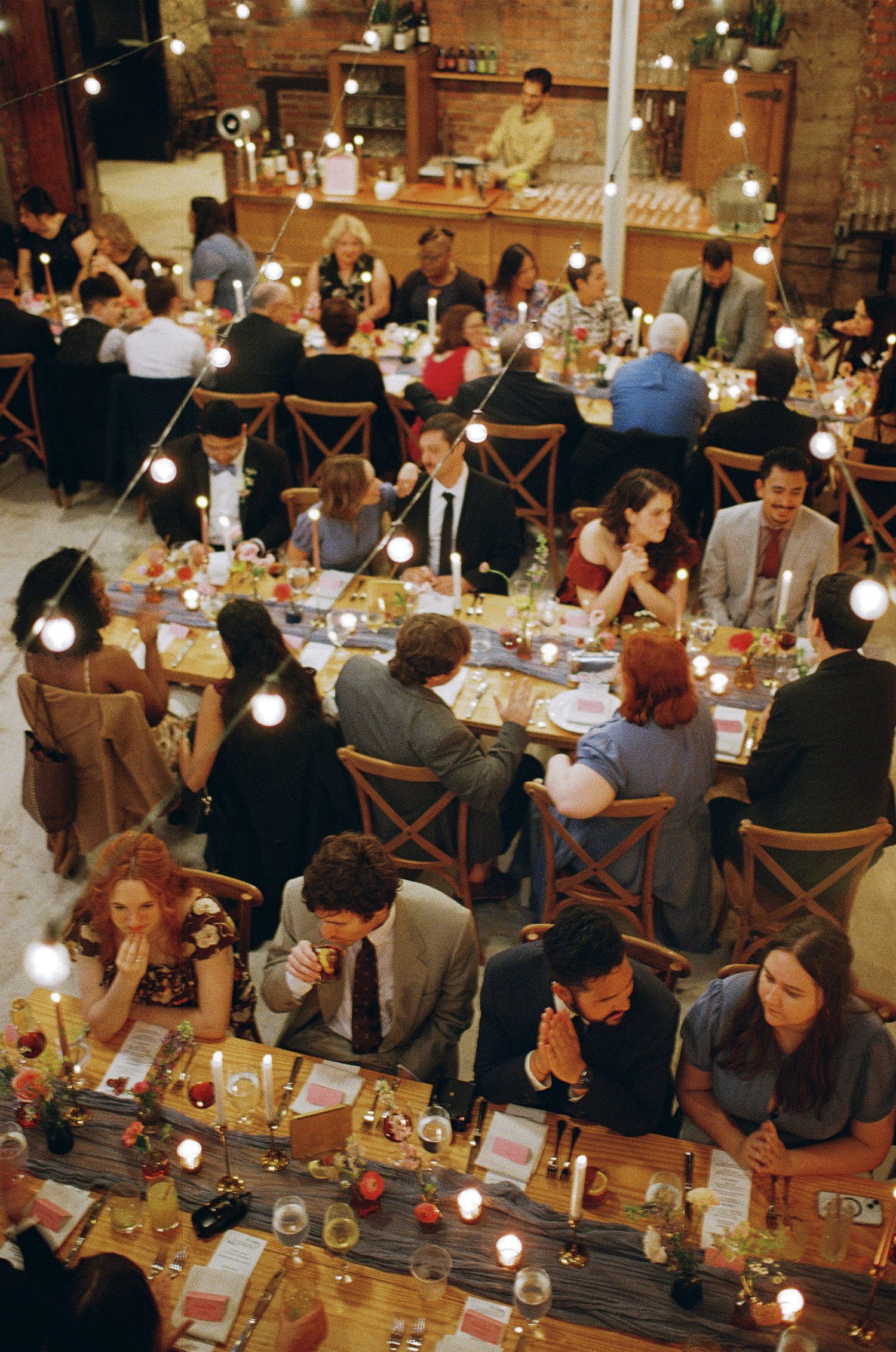 Large group of wedding guests seated at long tables in a rustic reception venue.