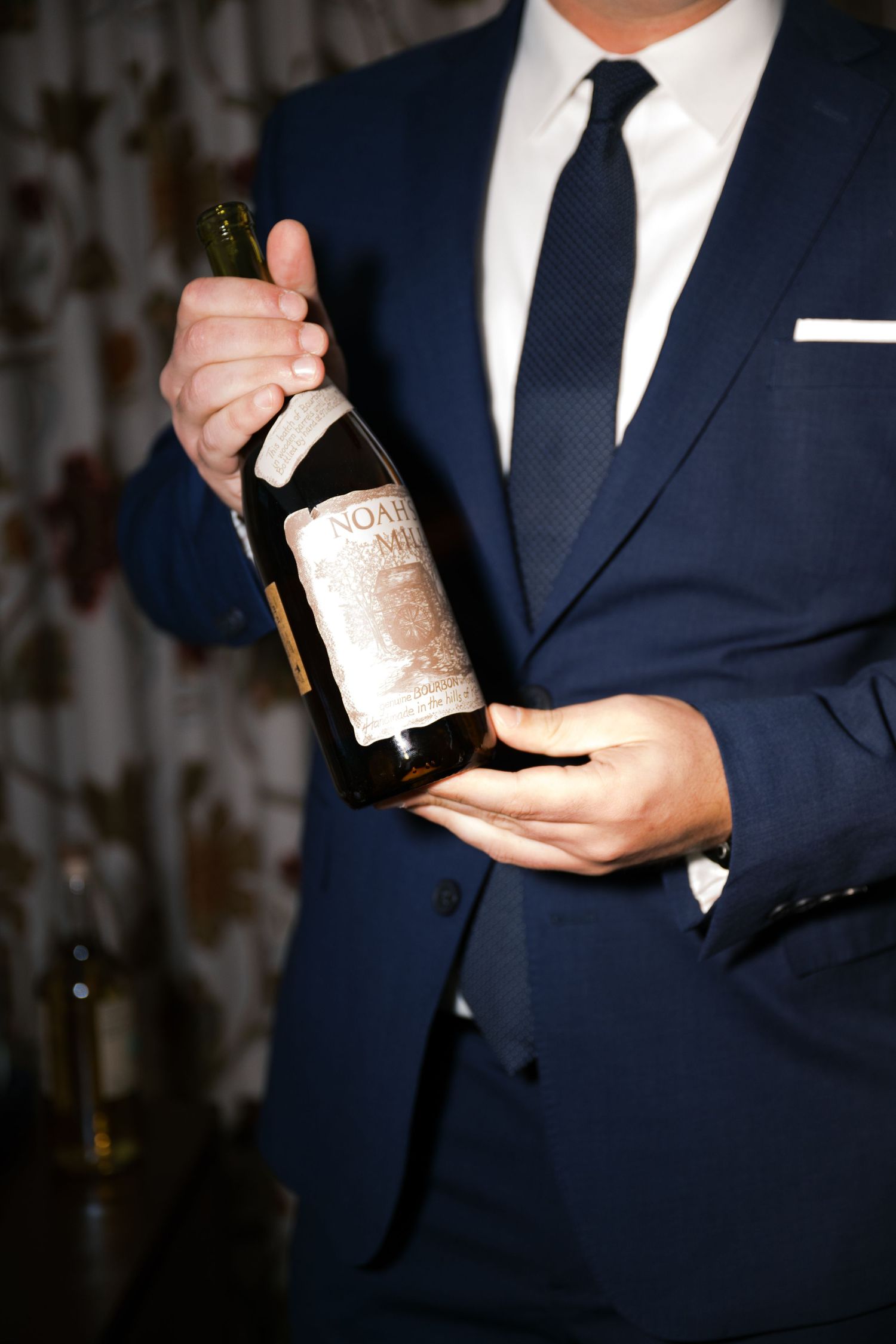 Well-dressed person in a navy blue suit holds a vintage wine bottle.