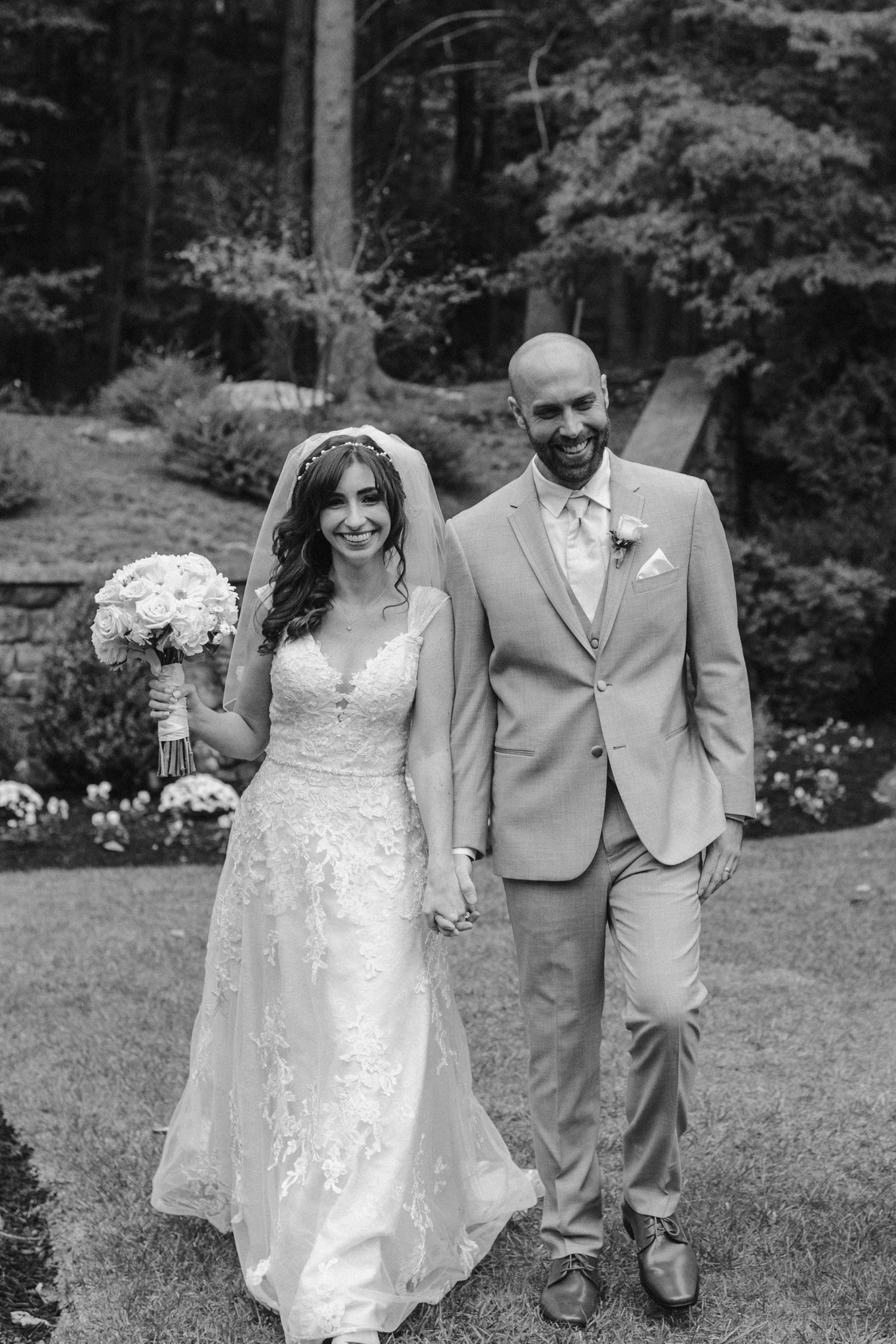 Black and white photo of newlyweds posing with bouquet in a garden setting.