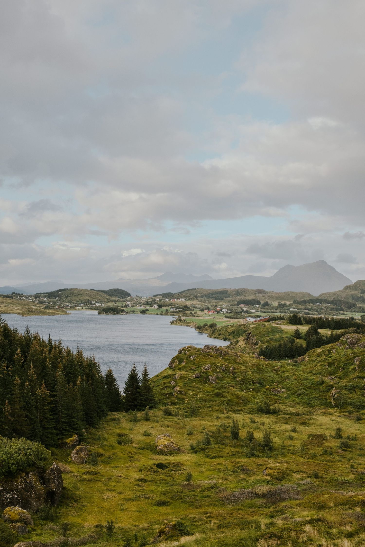 Coastal village nestled along a serene bay with mountains in the distance under cloudy skies.