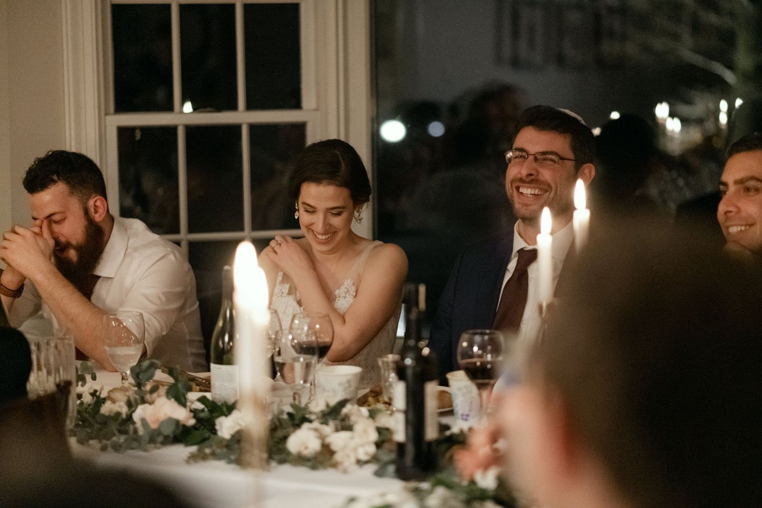 Joyful reactions during wedding reception speeches at elegant candlelit dinner.