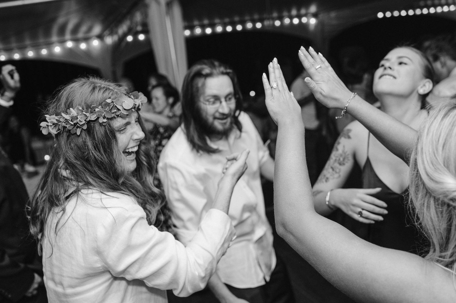 Party guests dancing and celebrating under tent lighting at an evening reception.