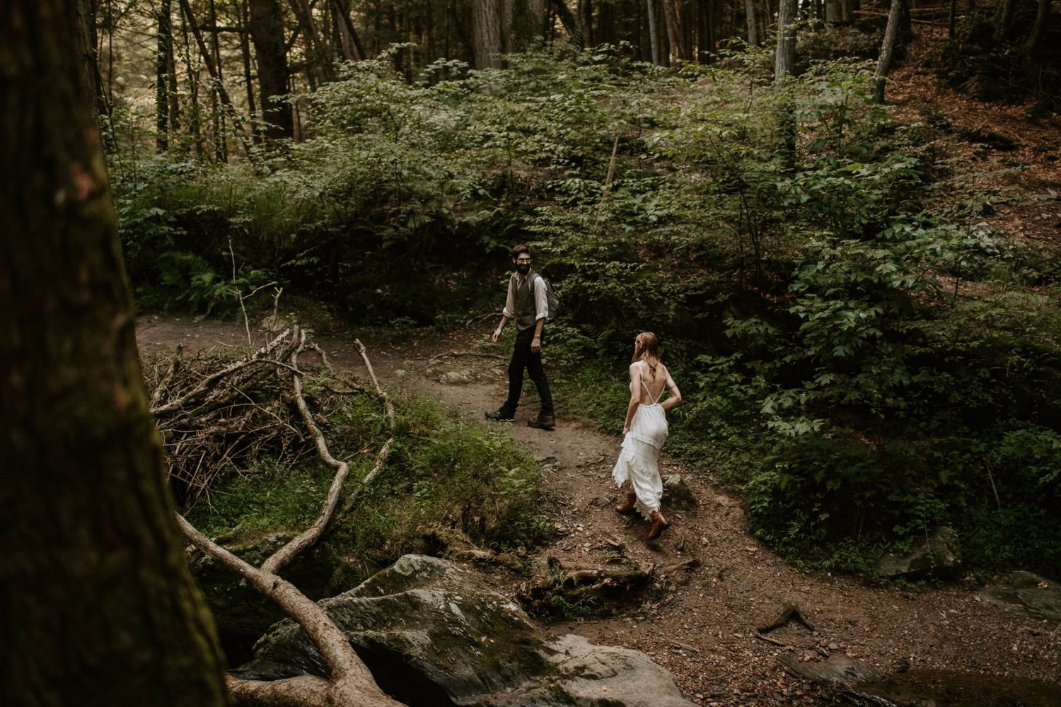 A couple walks along a rocky forest path during their intimate wedding celebration.