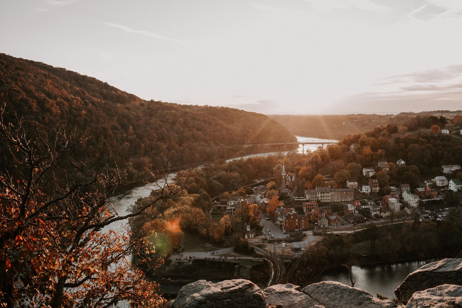 Aerial view of a winding river through autumn hills with small town nestled in valley at sunset.