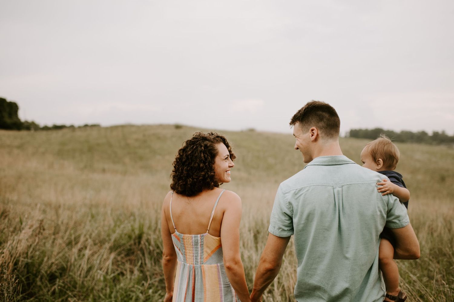 Black and white portrait of family walking through meadow with rolling hills in background.