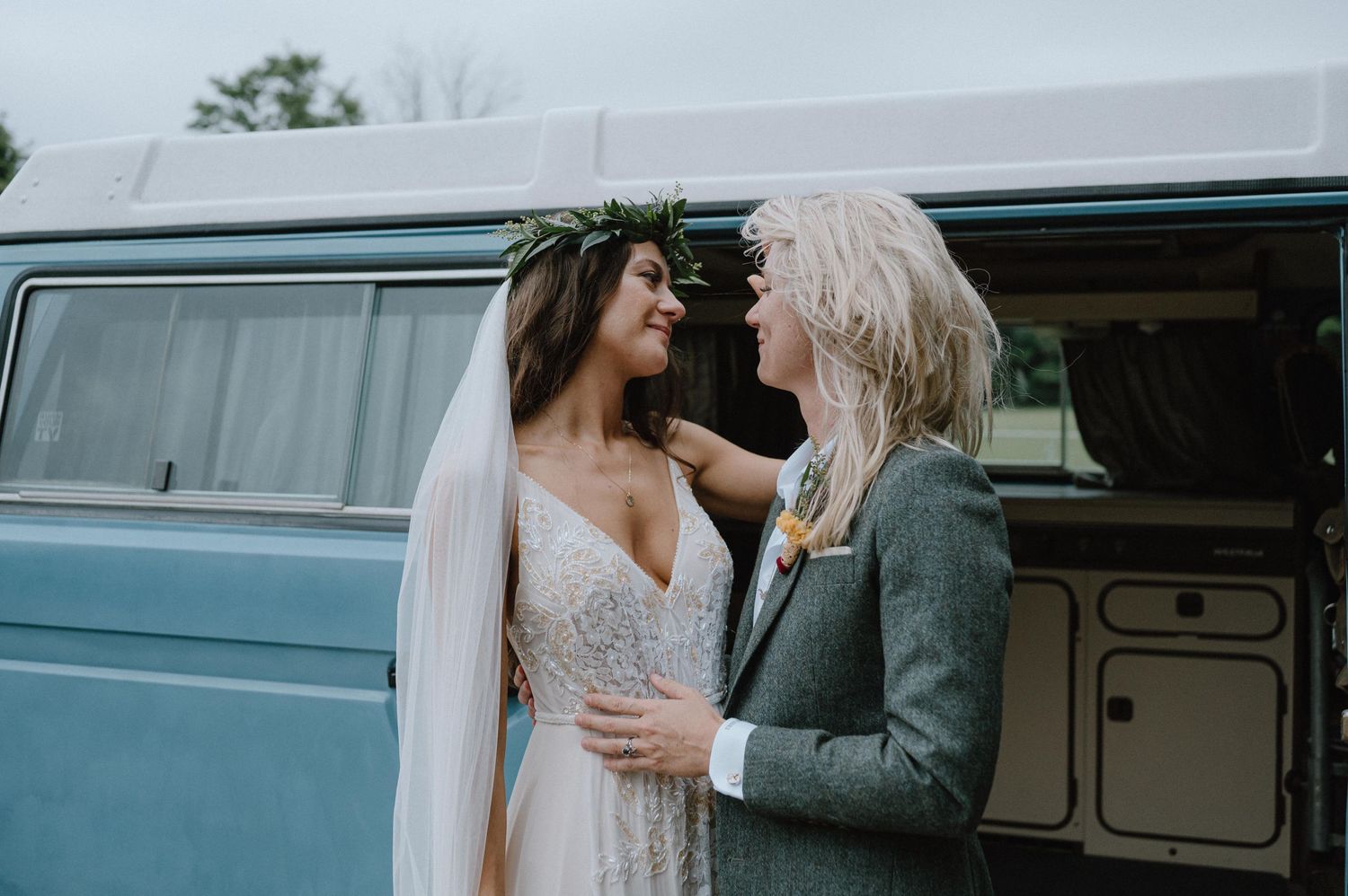 A couple shares an intimate moment in front of a light blue vintage VW van.