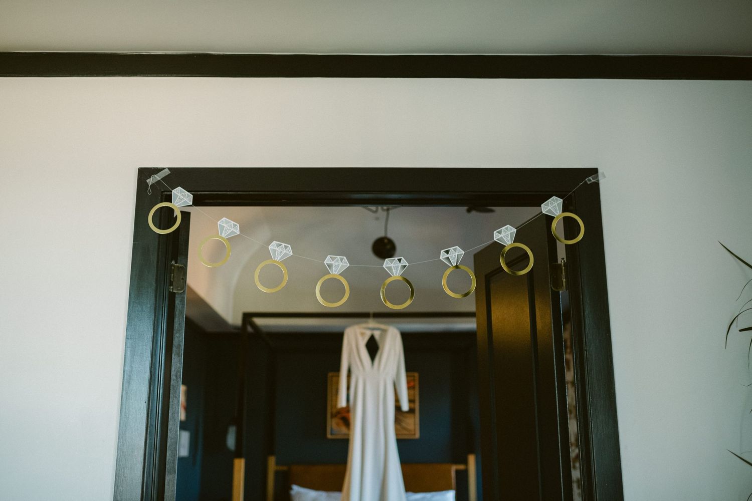 White wedding dress hanging in doorway with decorative lights above.
